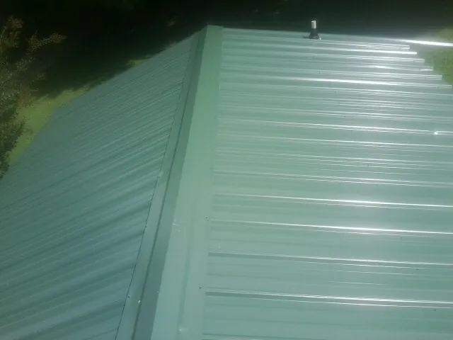 New green metal panels meeting at the ridge of a roof — Flat Roof Repair work by our crew in Bloomington